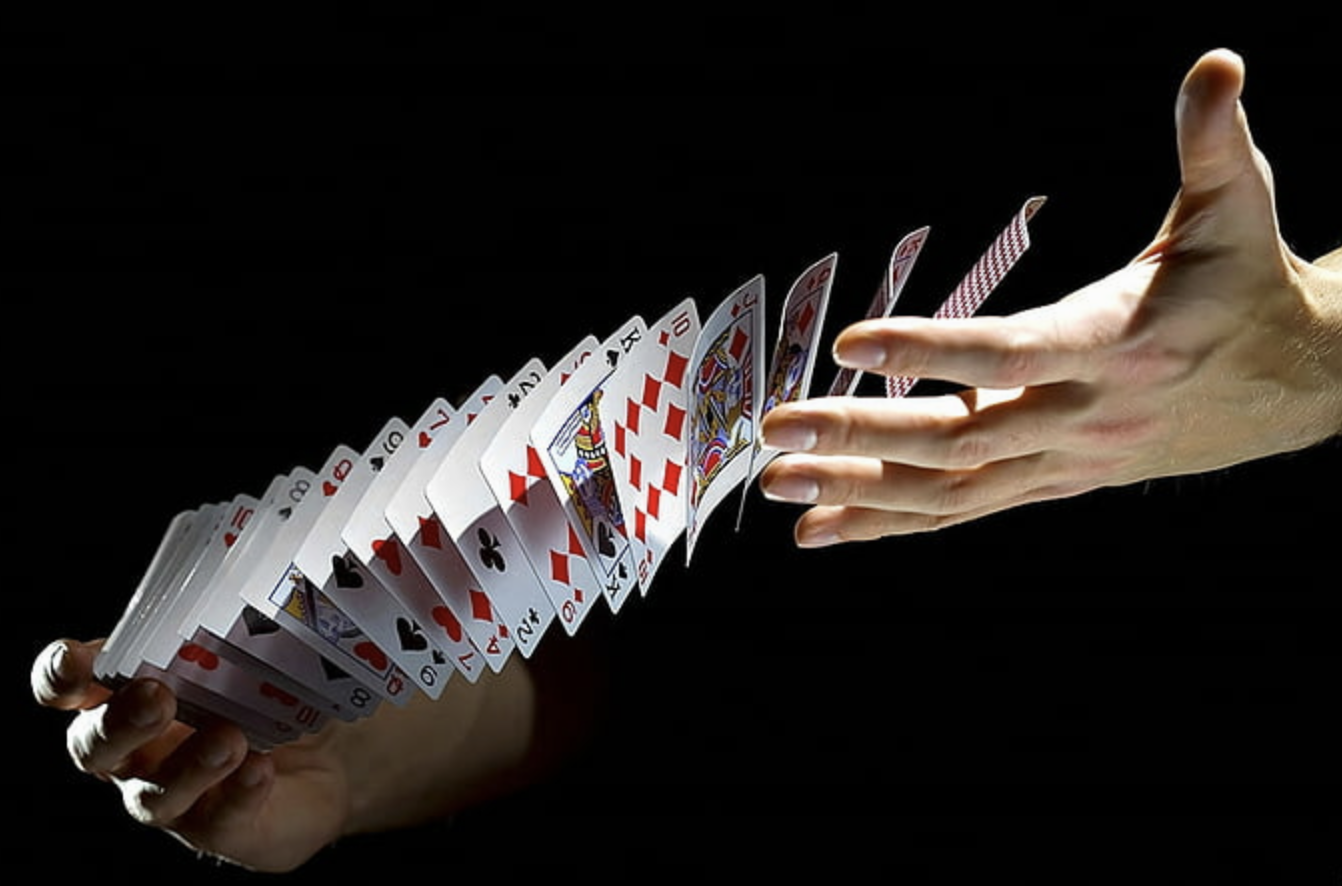 A magician's hands displaying a ribbon spread of playing cards against a black background